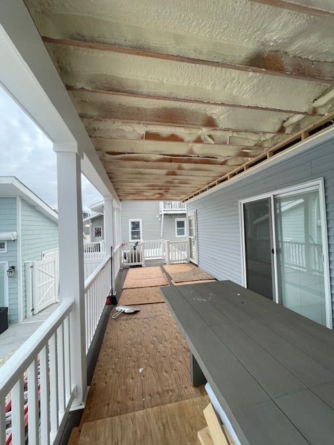 Covered porch under renovation with exposed ceiling joists, gray siding, and construction materials on the floor.