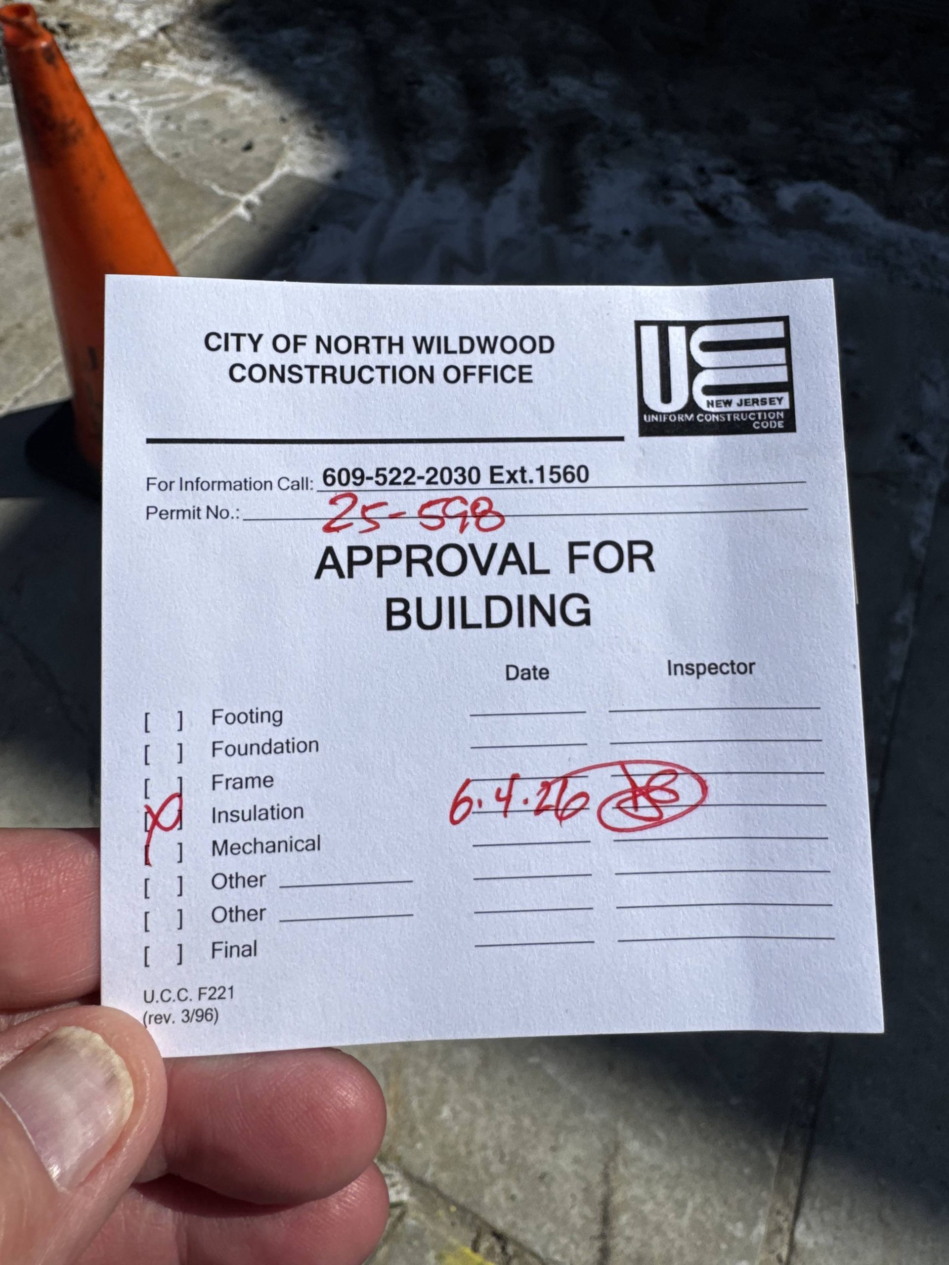 Hand holding a City of North Wilkesboro building approval form with handwritten notes and an orange cone in the background