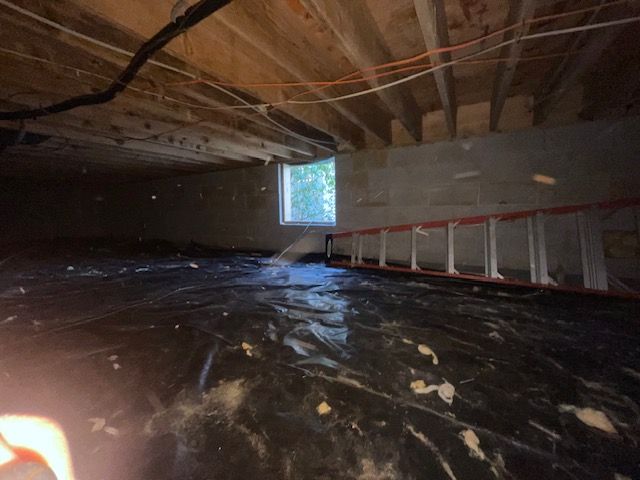 Unfinished attic crawlspace with plastic-covered floor, exposed beams, and a small window.
