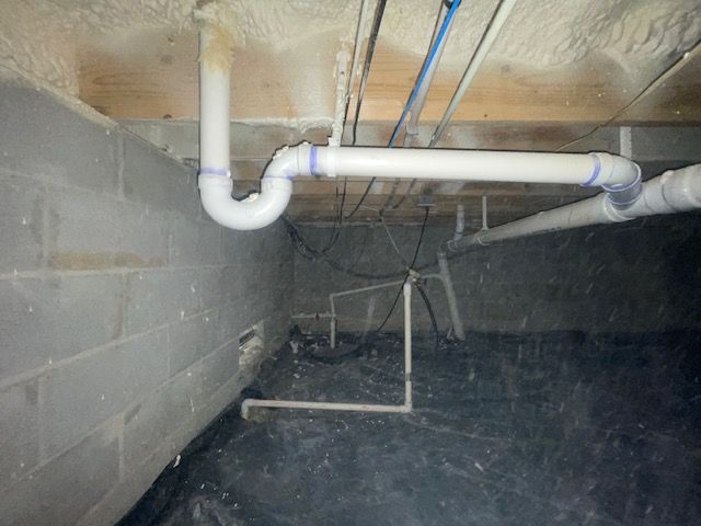 Basement crawlspace with cinderblock walls, exposed pipes, and a concrete floor under the house