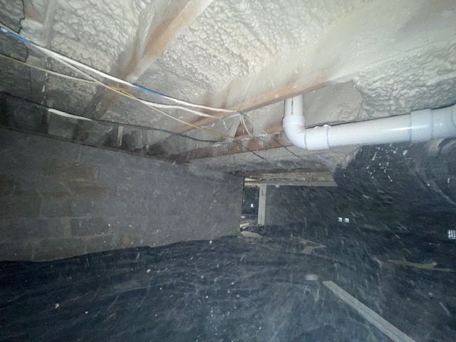 Crawlspace with insulation lining the floor and ceiling, and white PVC pipes running along the right side.
