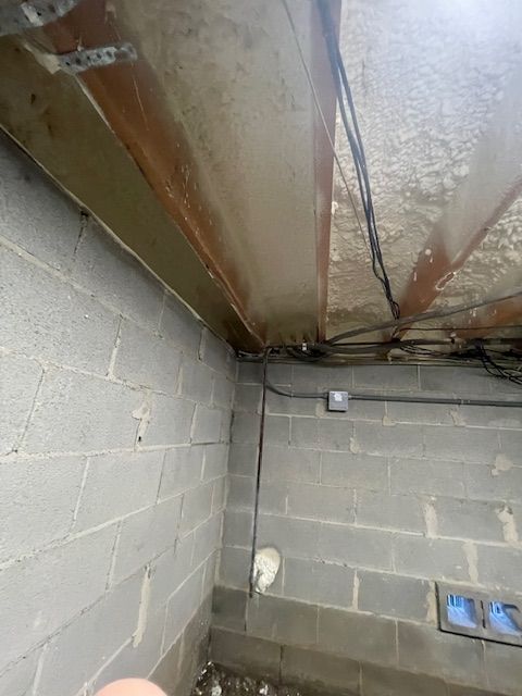 Damp basement corner with cinderblock walls, exposed ceiling beams, pipes, and utility fixtures