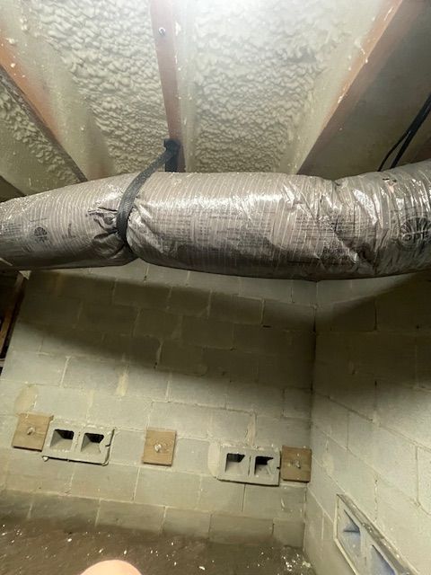 Insulated HVAC ductwork runs across a cinder block basement wall and ceiling.