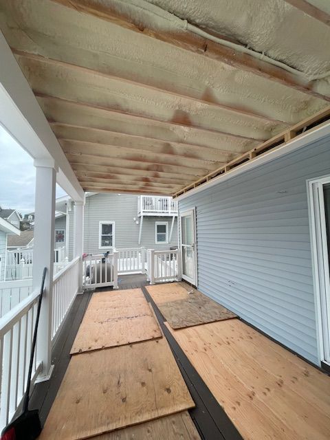 Covered porch with plywood floor panels and unfinished ceiling beside a gray house