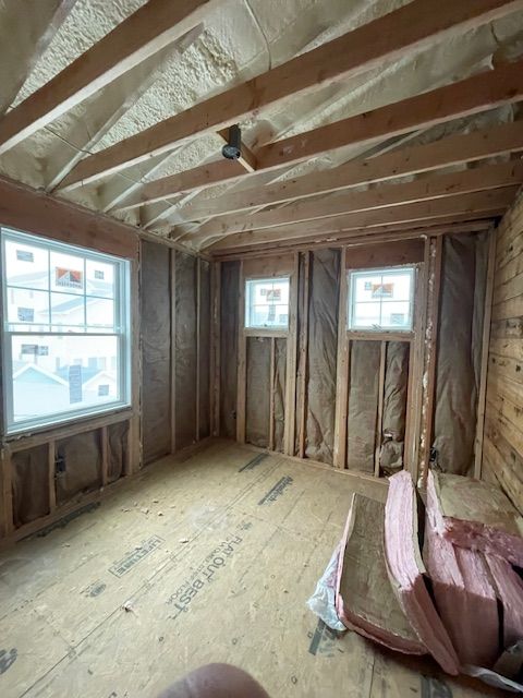 Unfinished room with exposed wood framing, two windows, and stacked pink insulation boards on the floor