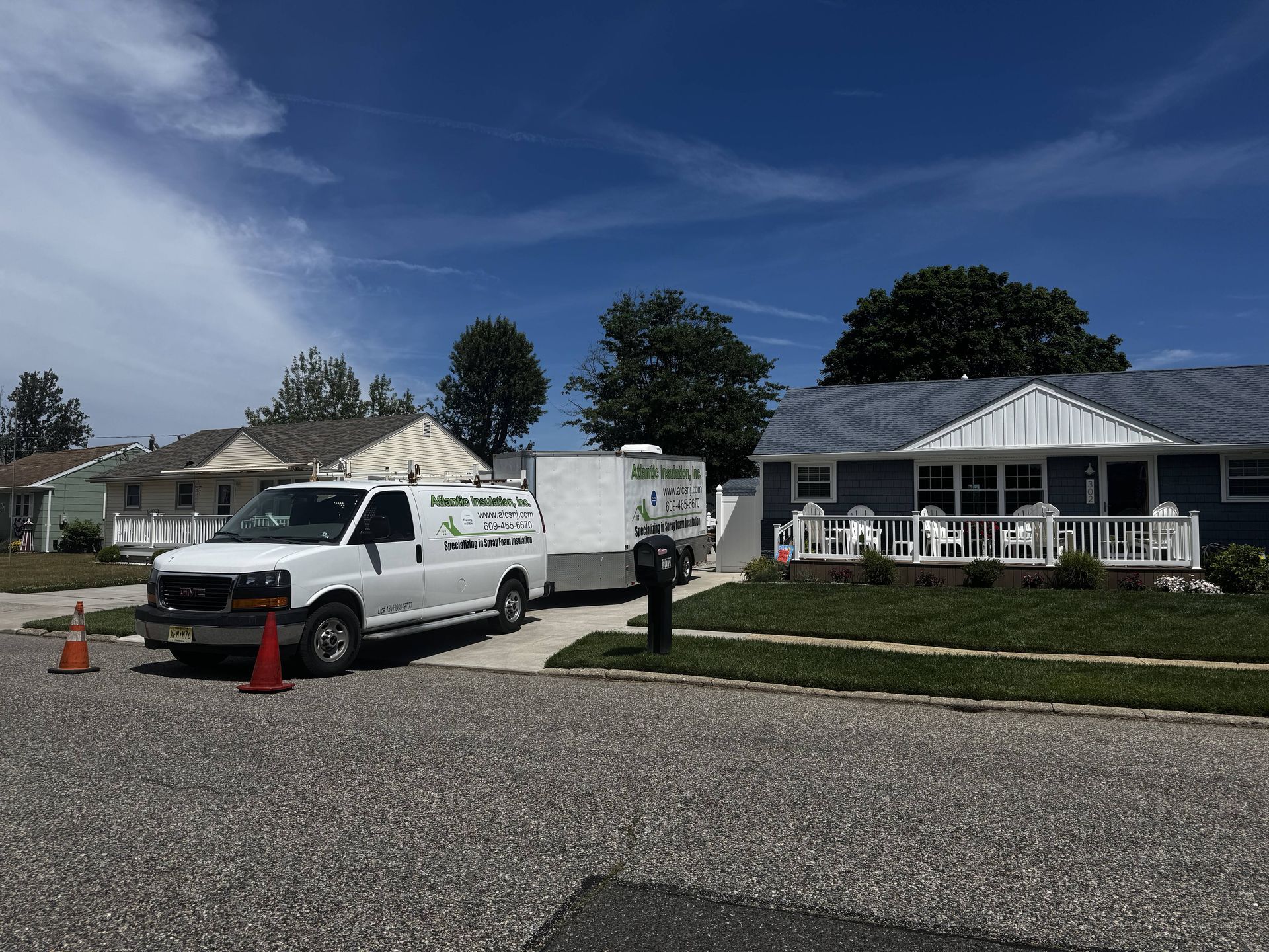 White utility truck parked on a gravel street beside a house with cones and a person standing nearby