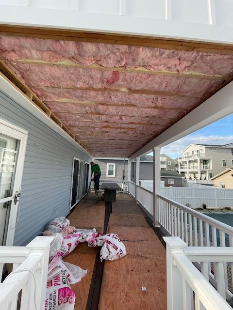 Covered porch under construction with pink insulation exposed in the ceiling and building materials on the floor
