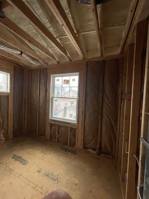 Unfinished wooden room interior with exposed framing, insulation, and two windows.