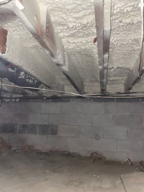Unfinished basement with cinder block wall and spray-foam insulation between exposed ceiling joists.