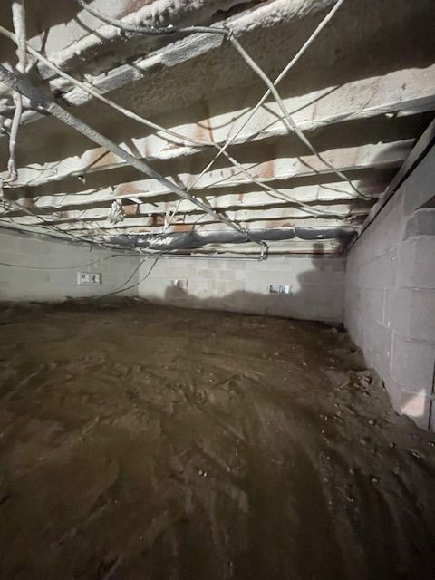 Flooded basement with exposed ceiling pipes and muddy standing water