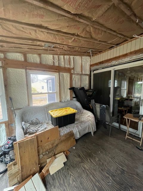 Cluttered covered porch with a gray couch, yellow blanket, wood boards, and sliding glass doors