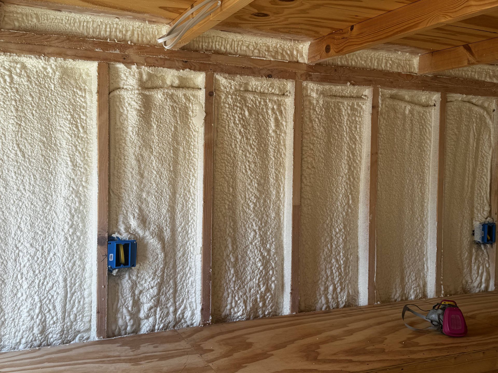 Insulated unfinished room with spray foam walls, exposed rafters, electrical boxes, and a bucket on the floor