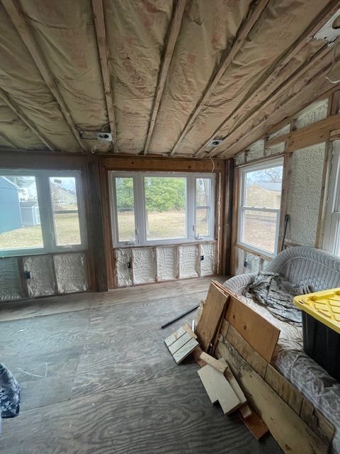 Unfinished room with exposed wood walls and ceiling, windows, and stacked construction materials.