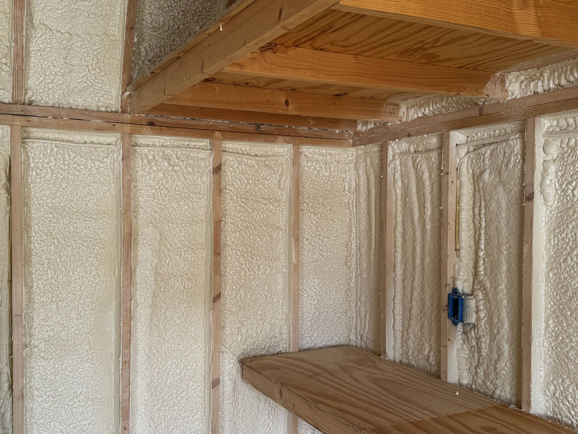 Partially finished room with insulated walls, exposed wooden beams, and a small wooden platform
