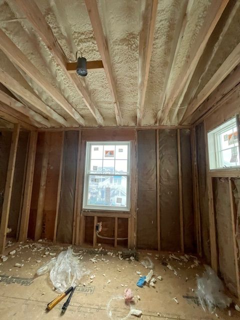 Unfinished room with exposed insulation, wood framing, two windows, and construction debris on the floor