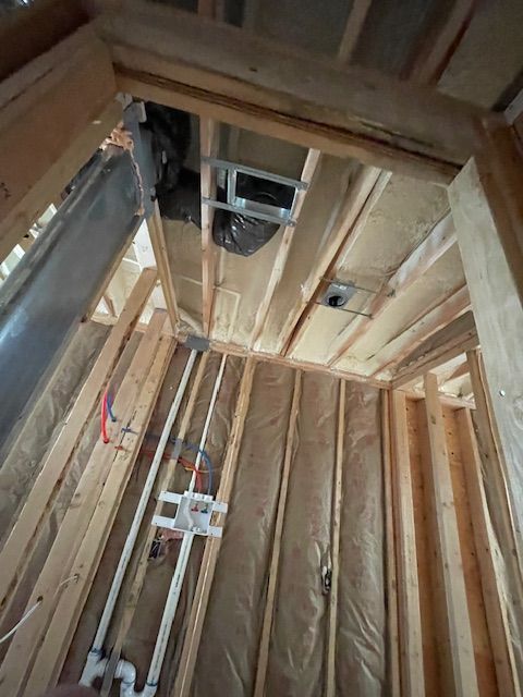 Unfinished attic with exposed wooden framing, insulation, and visible plumbing and electrical wiring.