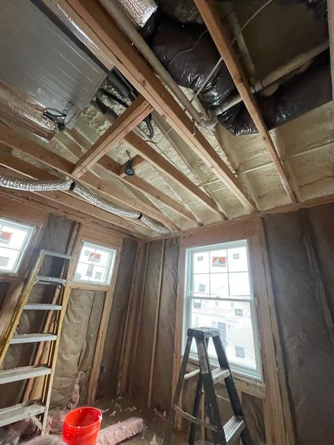 Partially renovated room with exposed ceiling beams, ladder, windows, and a red bucket on the floor