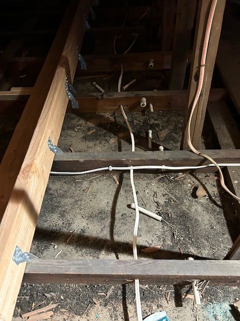 Exposed attic framing with loose electrical wires and insulation between wooden joists