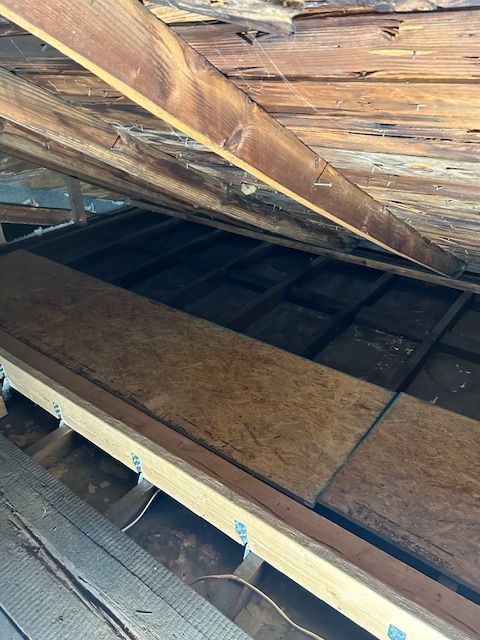 Wooden attic rafters and insulation boards with visible wiring in a dim, unfinished crawlspace