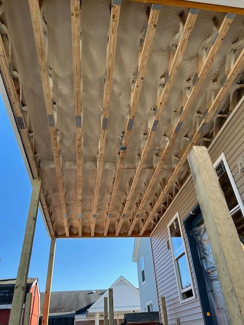 Low-angle view of unfinished wooden porch framing attached to a house under a clear blue sky