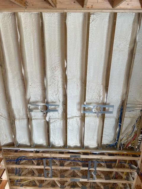 Ceiling showing white spray foam insulation between exposed wooden joists and metal brackets