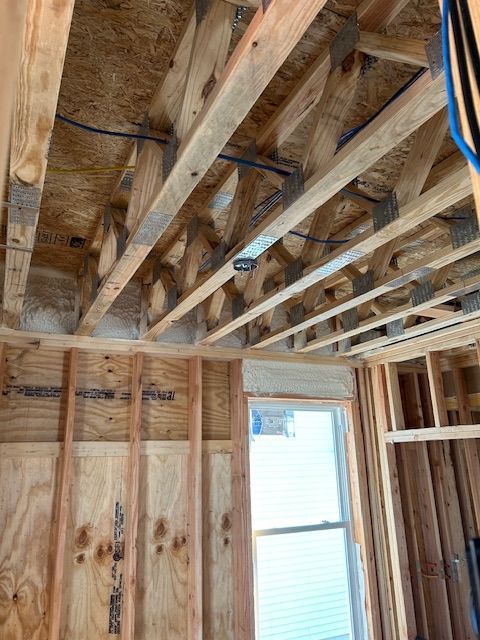 Interior of unfinished room with exposed wooden ceiling joists, framing, insulation, and a window.