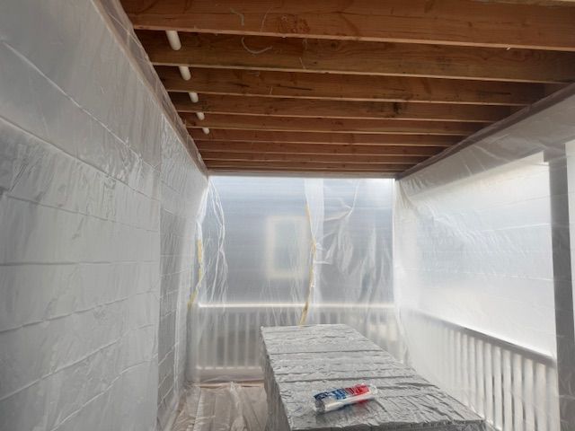 Covered porch under construction, with plastic sheeting on walls and a workbench in the foreground.