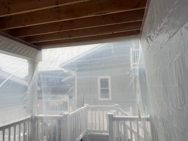 Snowy porch with white railing and wooden ceiling, looking out toward a neighboring house through heavy snowfall