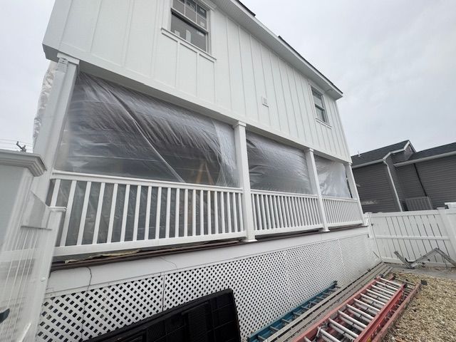 House exterior with white porch railings, plastic-covered windows, and a ladder leaning along the side.