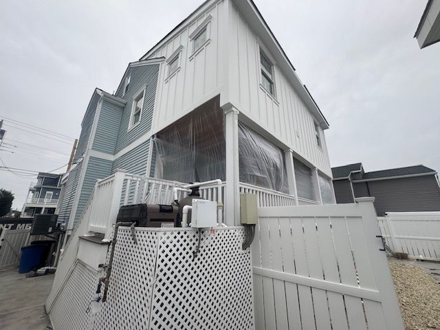 White two-story house with screened porch, lattice fence, and gravel yard under an overcast sky
