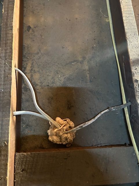 Knotted tan string with two white wires over a dark metal floor in a narrow compartment