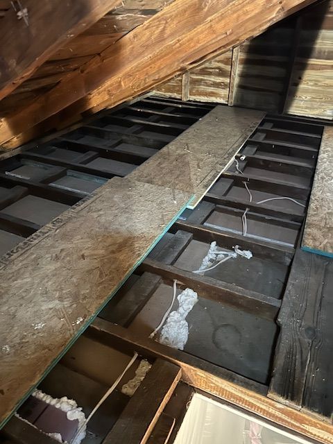 Interior attic with exposed wooden beams, open floor joists, and a narrow plank walkway.