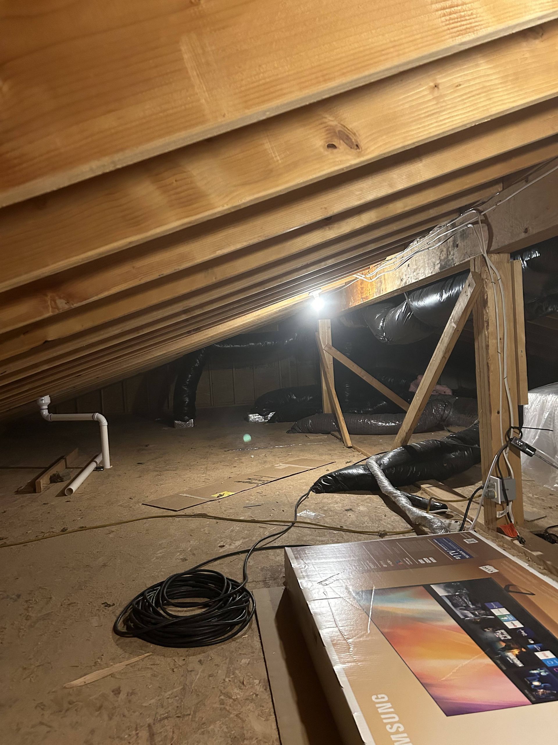 Crawlspace with exposed beams, dirt floor, scattered cables, and a bright light illuminating the area.