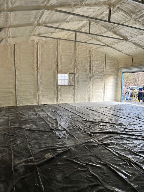 Insulated empty workshop with white walls, arched ceiling, black floor covering, and an open doorway.