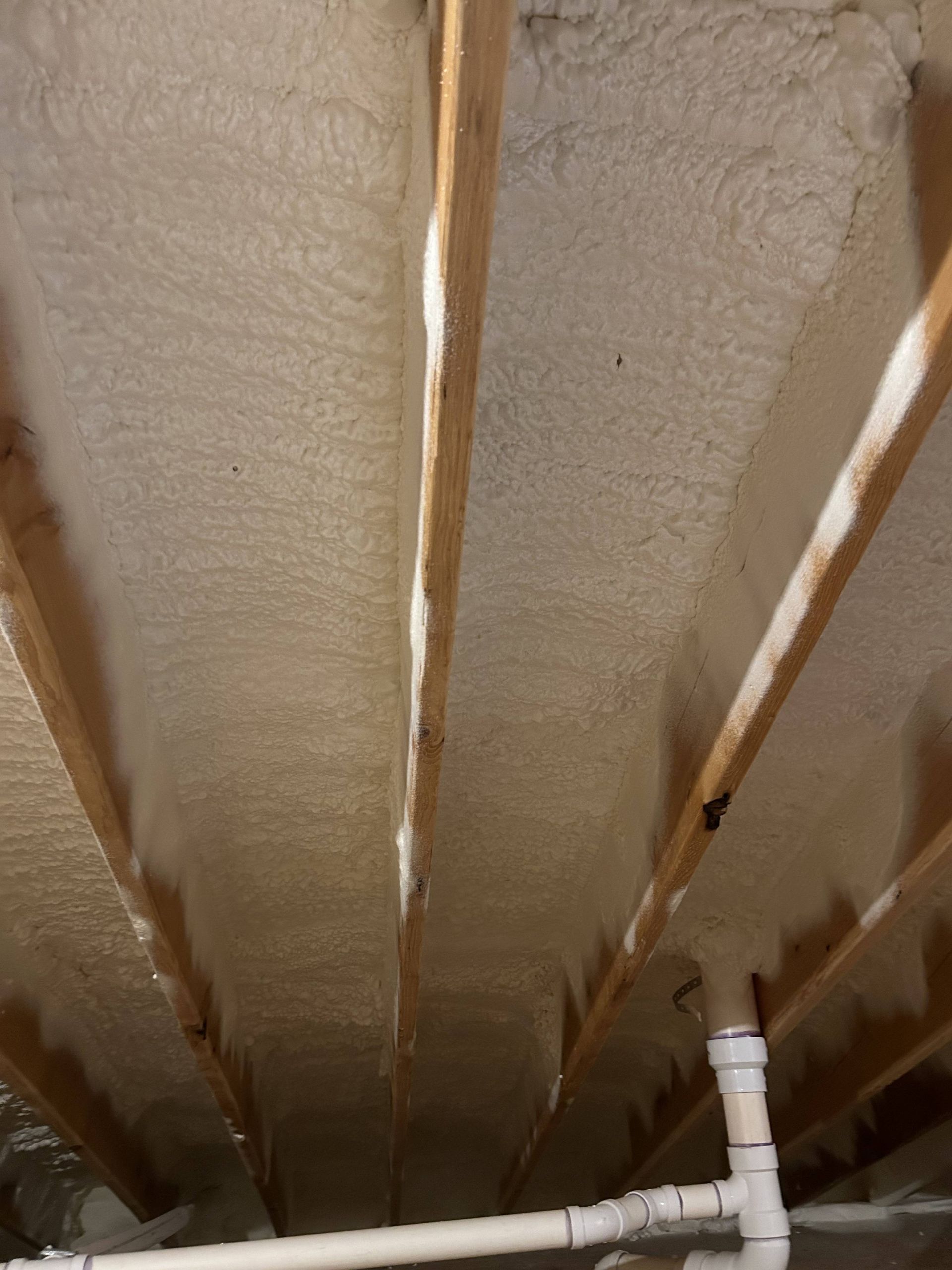 Insulated basement ceiling with exposed wooden joists and white plumbing pipe