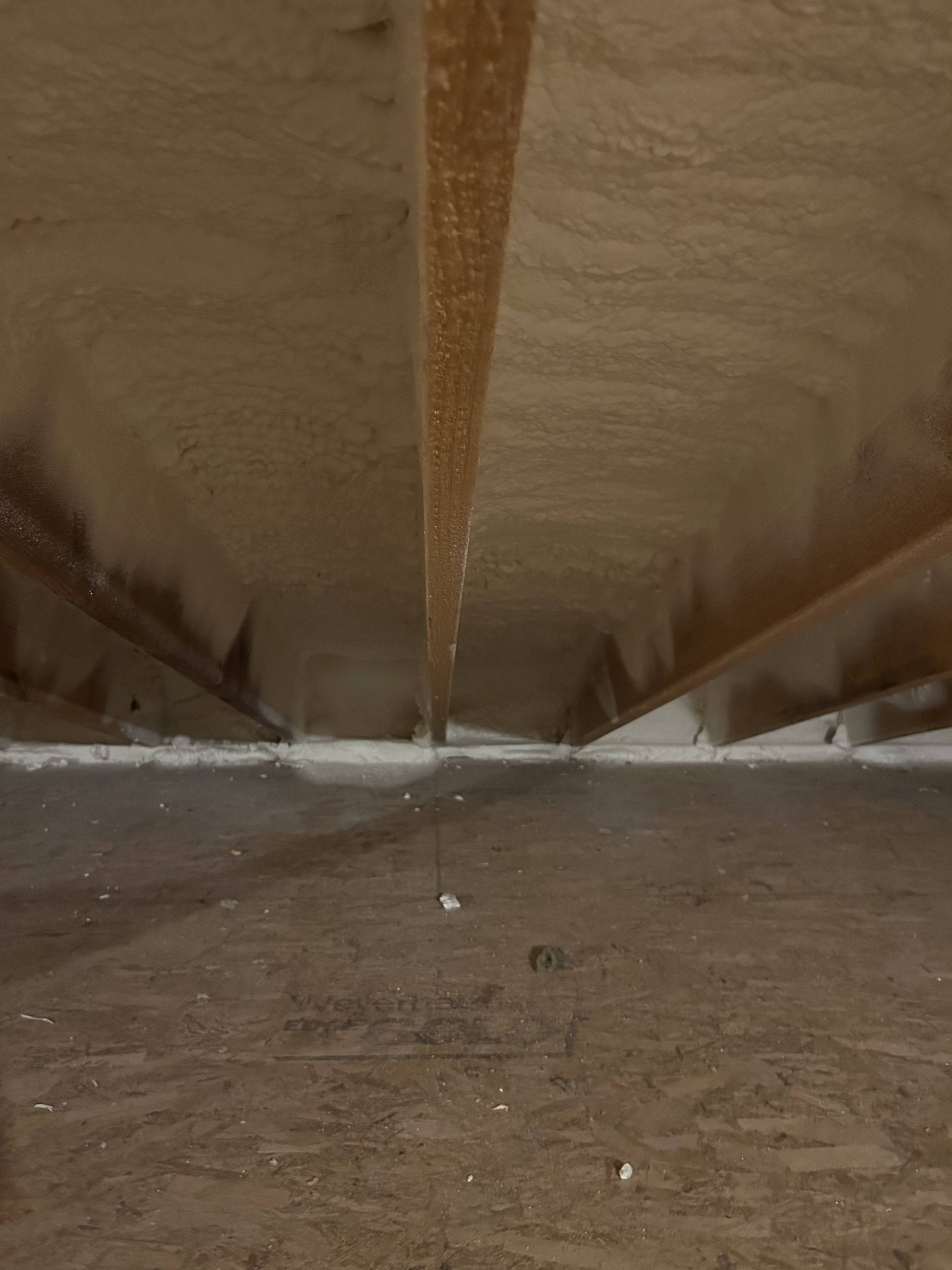 Inside an attic, a narrow view along the roof ridge with wooden rafters and insulation.