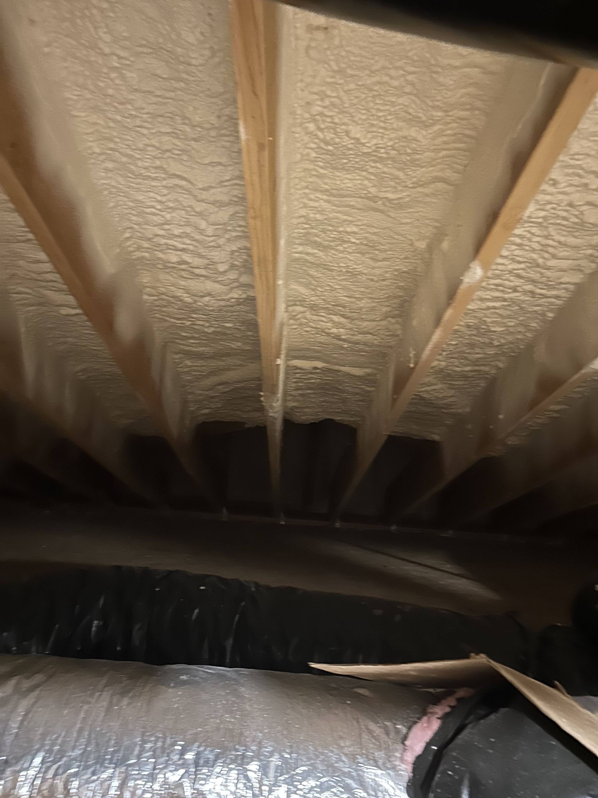 Insulated attic crawlspace with exposed wooden rafters and dark ducting below