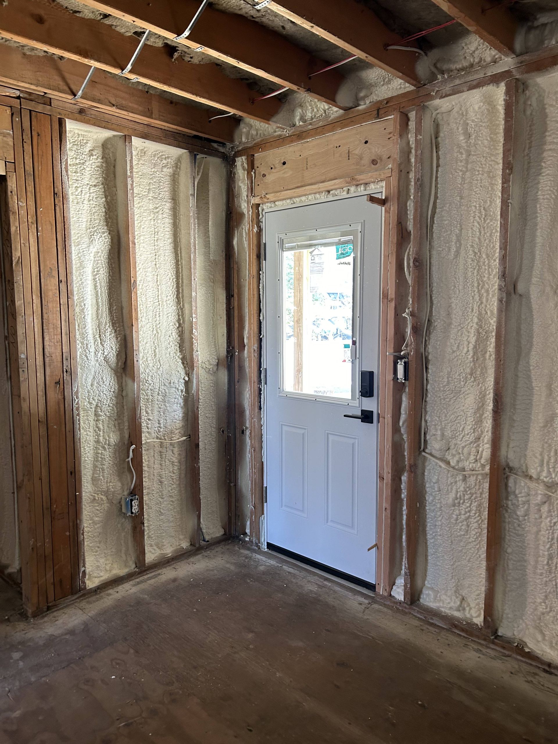 Unfinished room with exposed framing and insulation, featuring a white door and window.