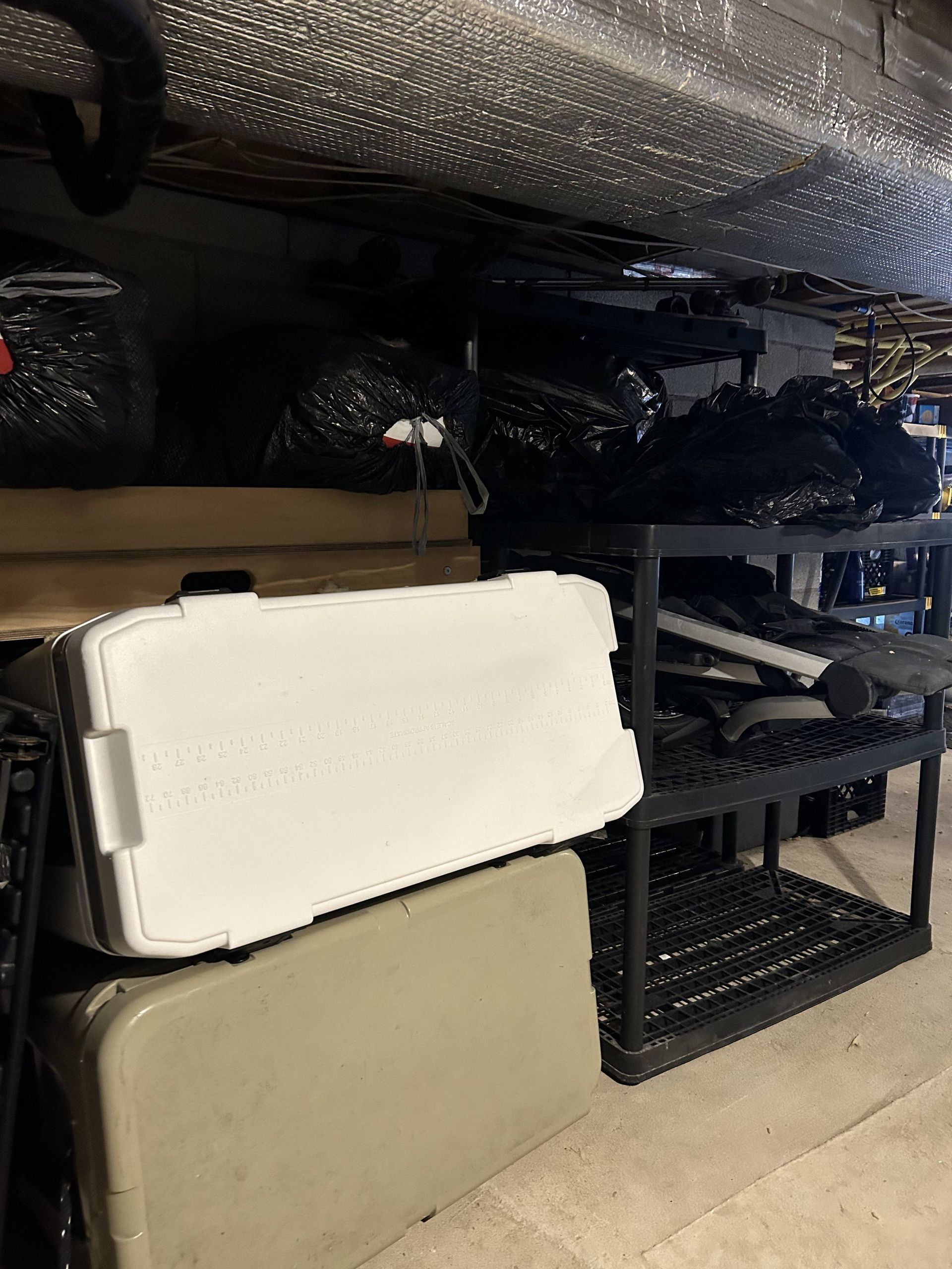 Shelved storage area with stacked foam mats, a white case, and black crates in a garage-like space