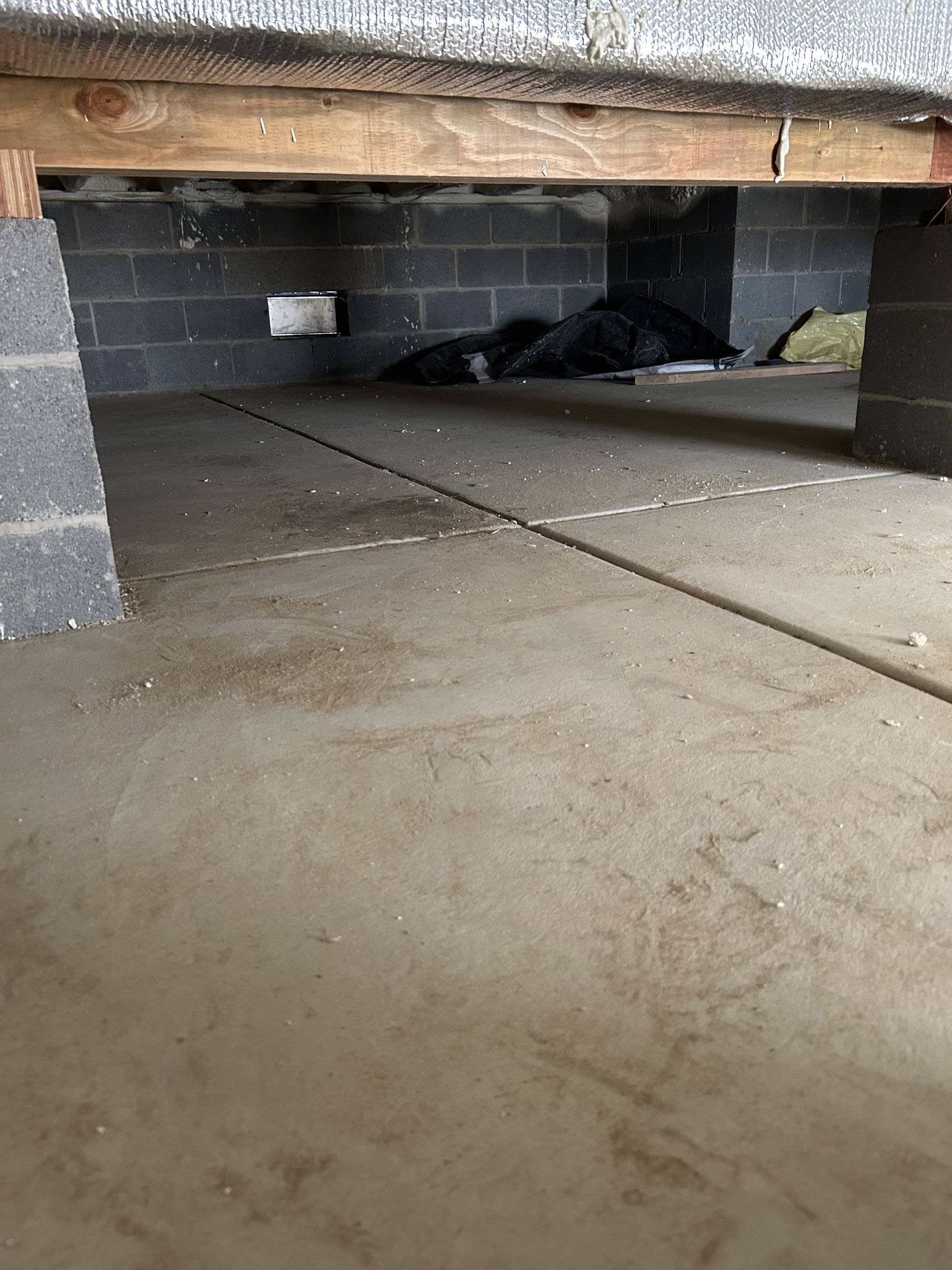Under a low wooden bed frame, with cinderblock supports and a concrete floor underneath.