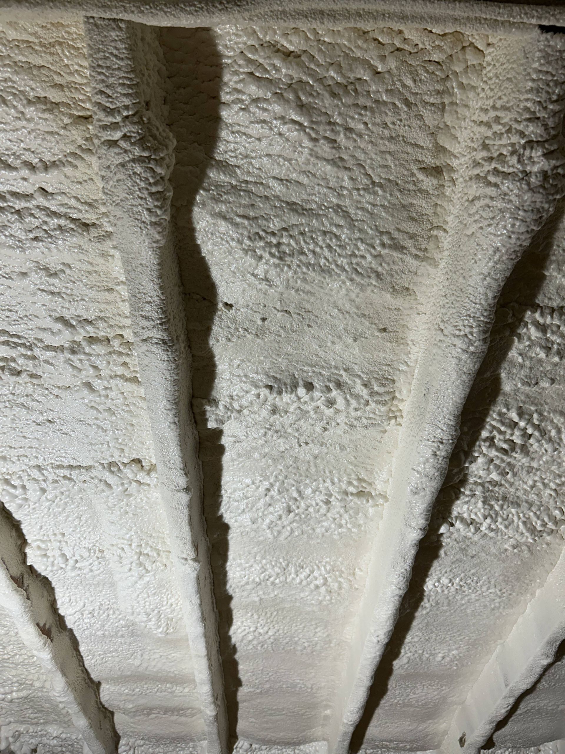 Close-up of white spray foam insulation filling gaps between roof rafters