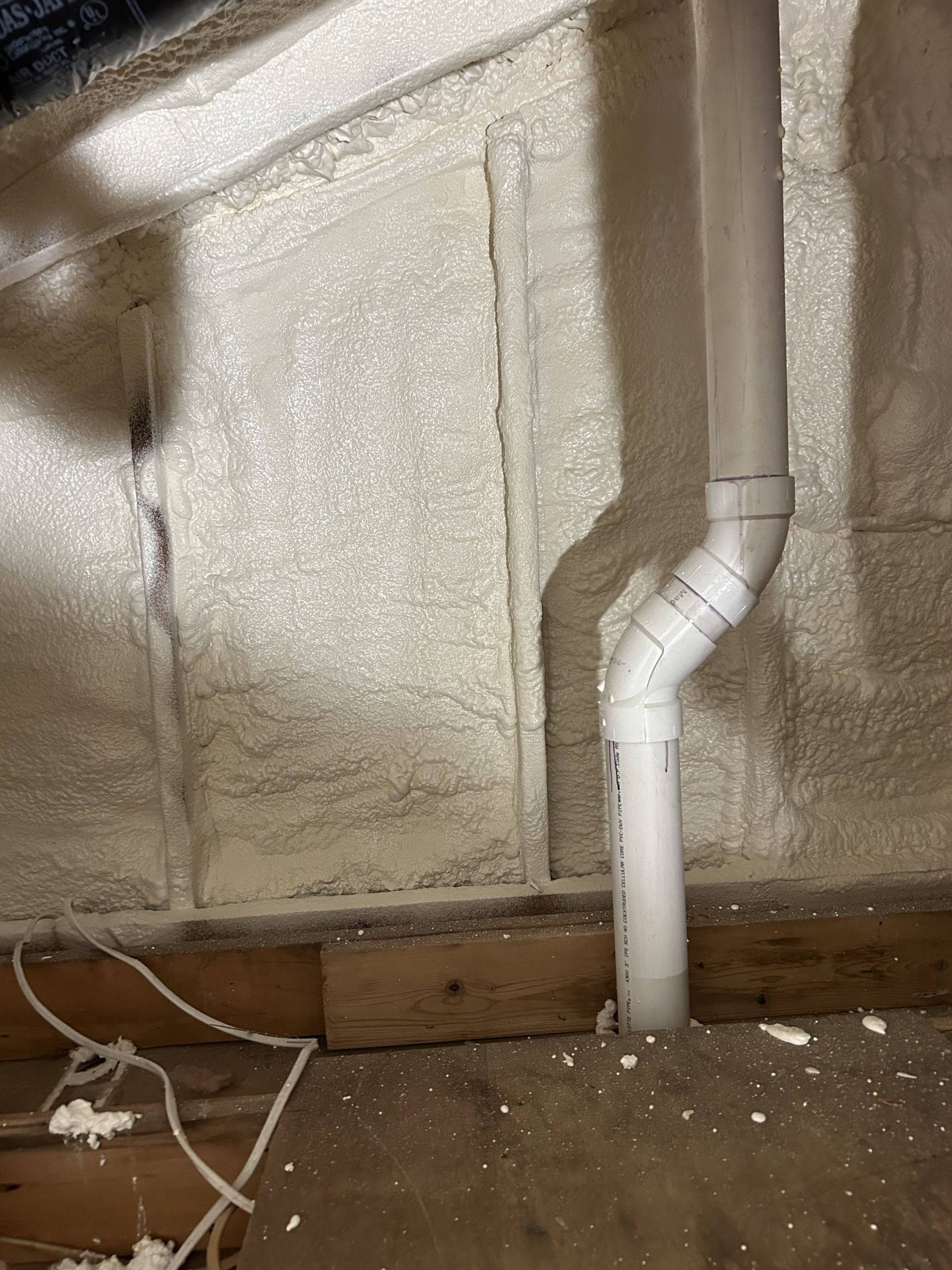 Insulated basement wall with white PVC pipe and exposed wires along the floor.