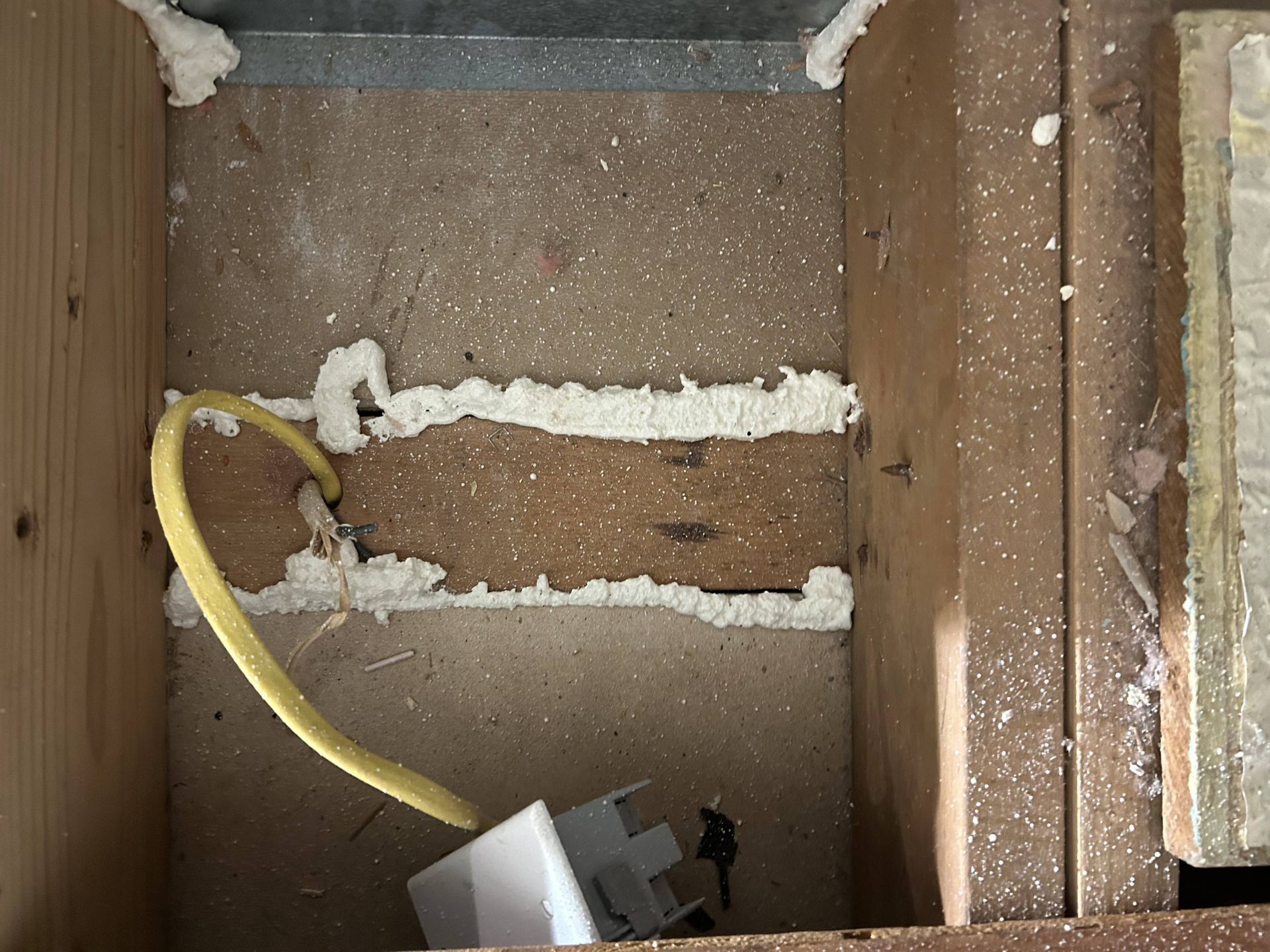 Open wooden wall cavity with yellow cable, white foam insulation, and a small electrical component at the bottom