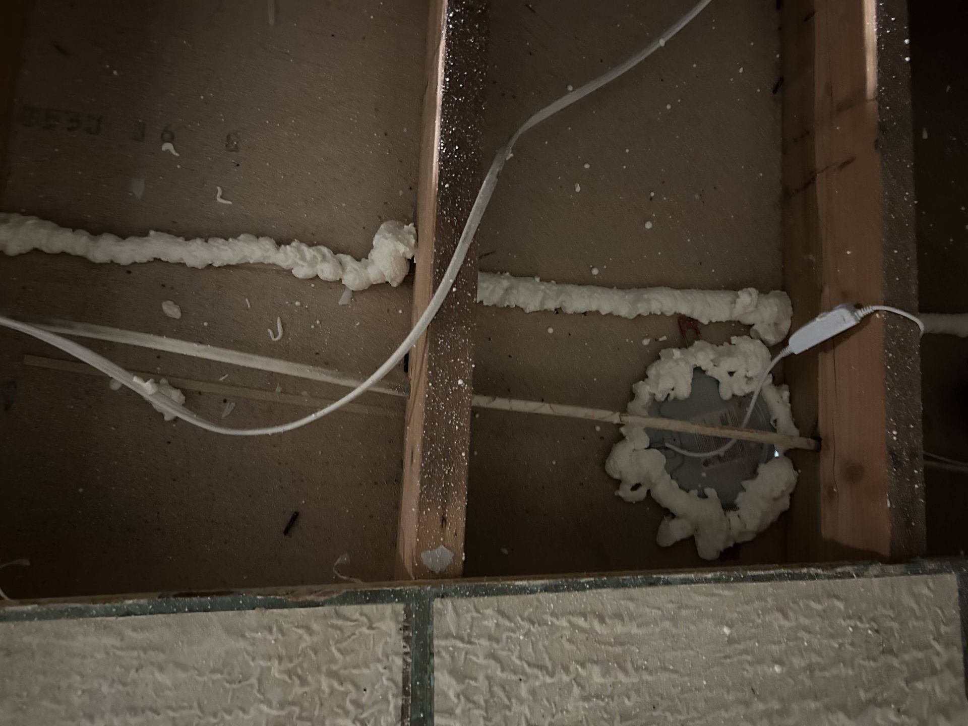 Open wall cavity with exposed wiring and spray foam insulation around pipes and studs