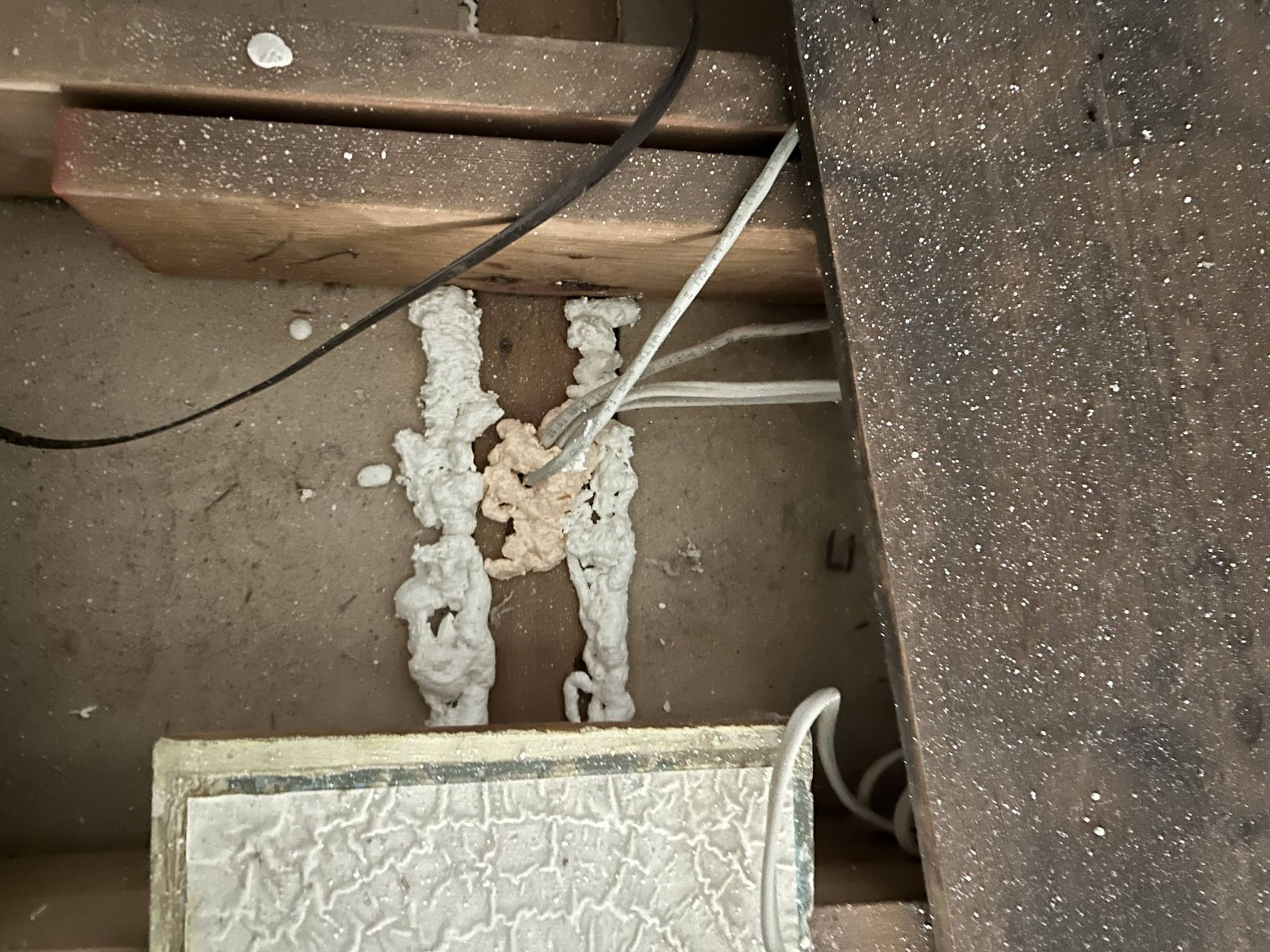 Undercounter area with white foam insulation around pipes and wires beneath a cabinet or appliance