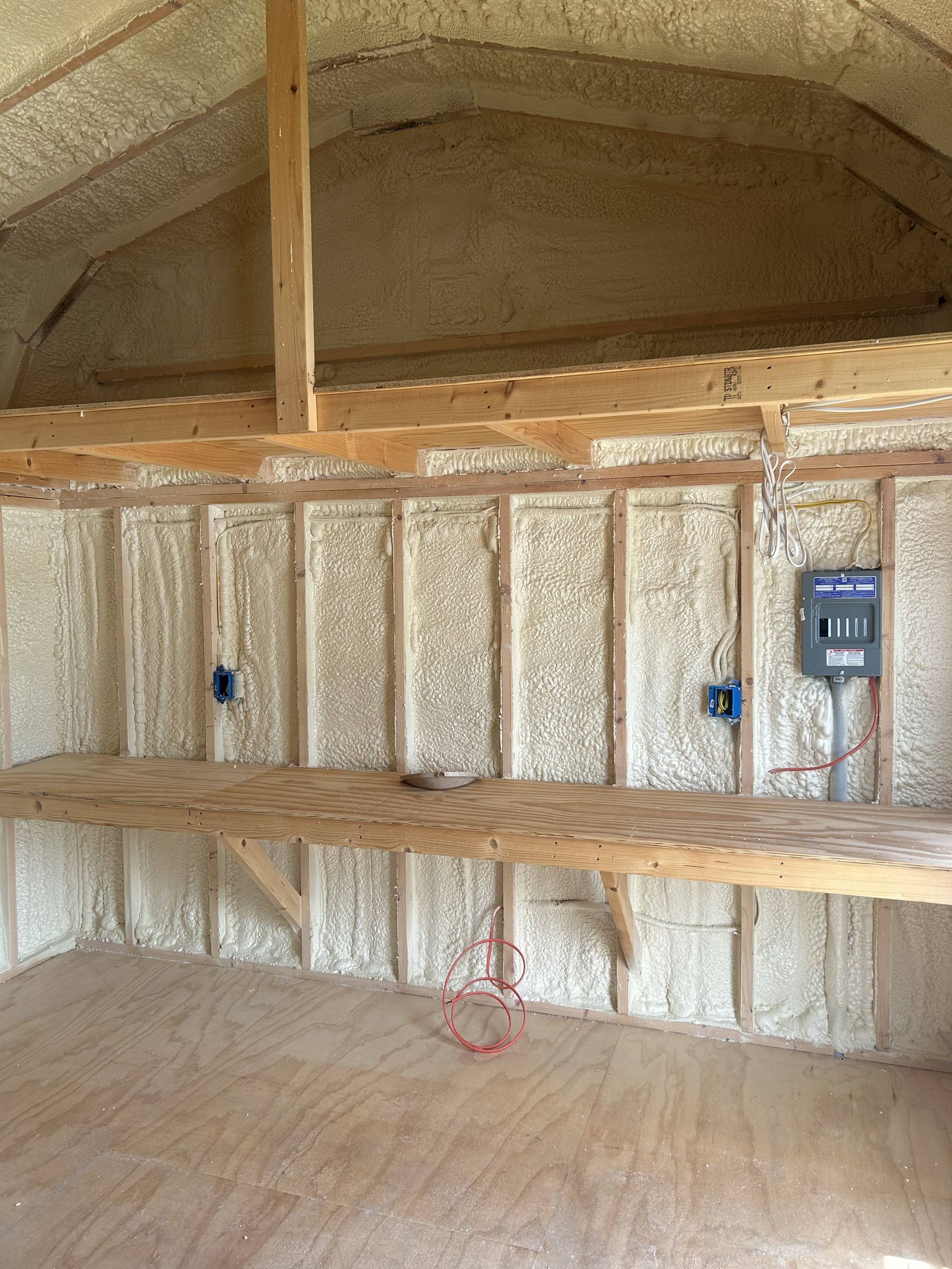 Empty unfinished room with exposed insulation, wooden framing, and a small electrical panel on the wall