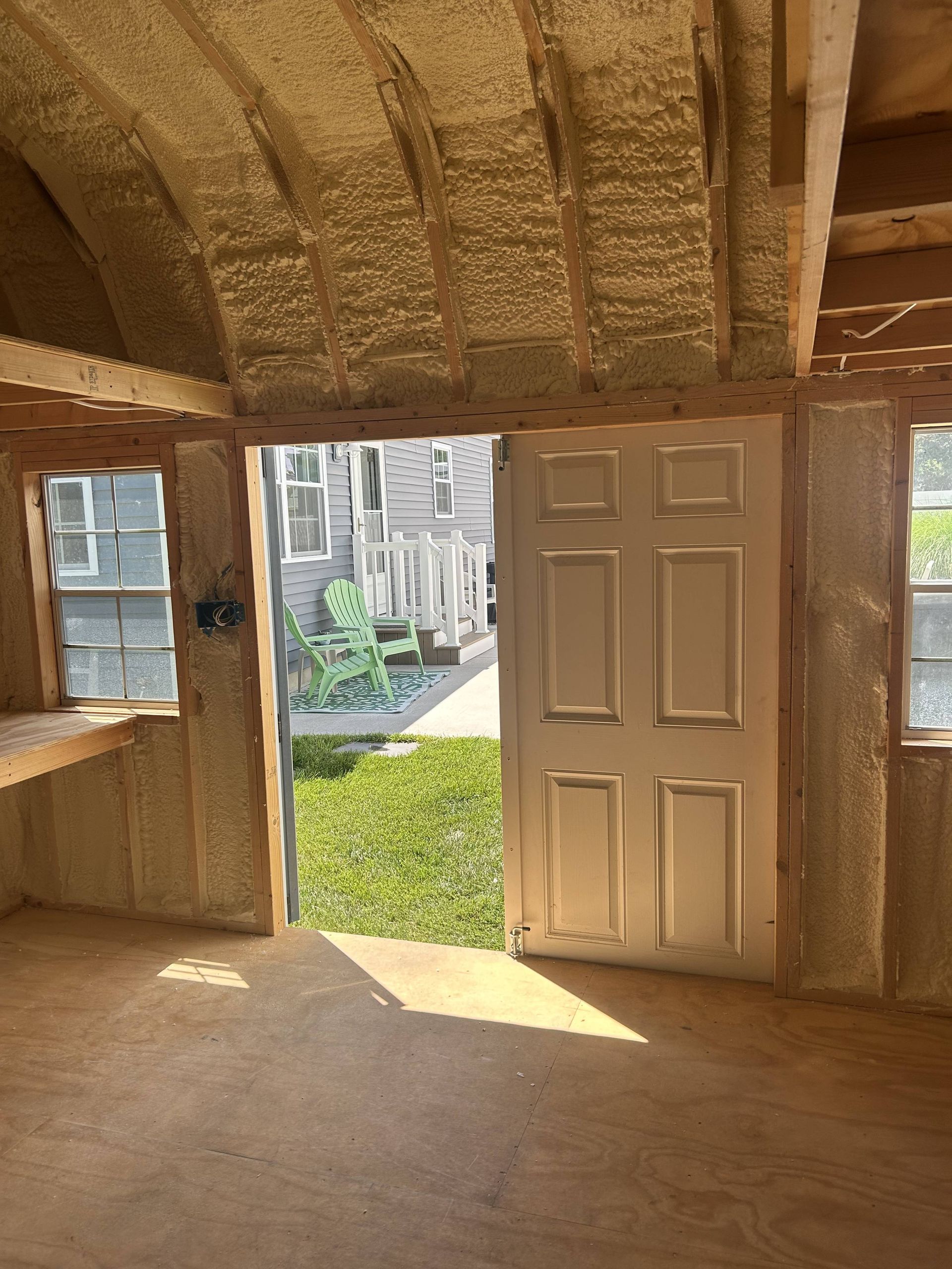 Rustic room with open door and window overlooking a sunlit courtyard and city buildings.