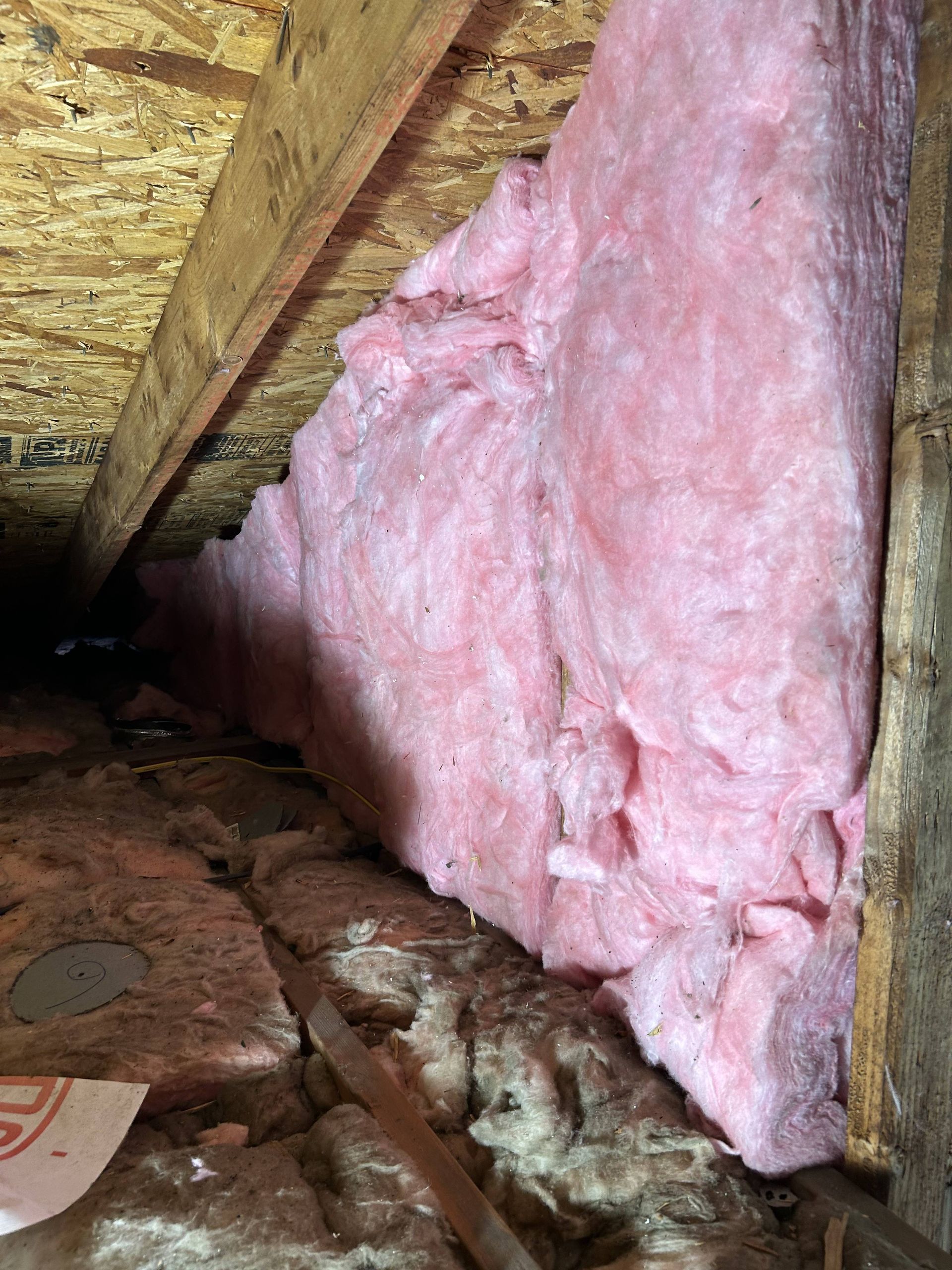 Pink fiberglass insulation inside an attic crawlspace under wooden rafters