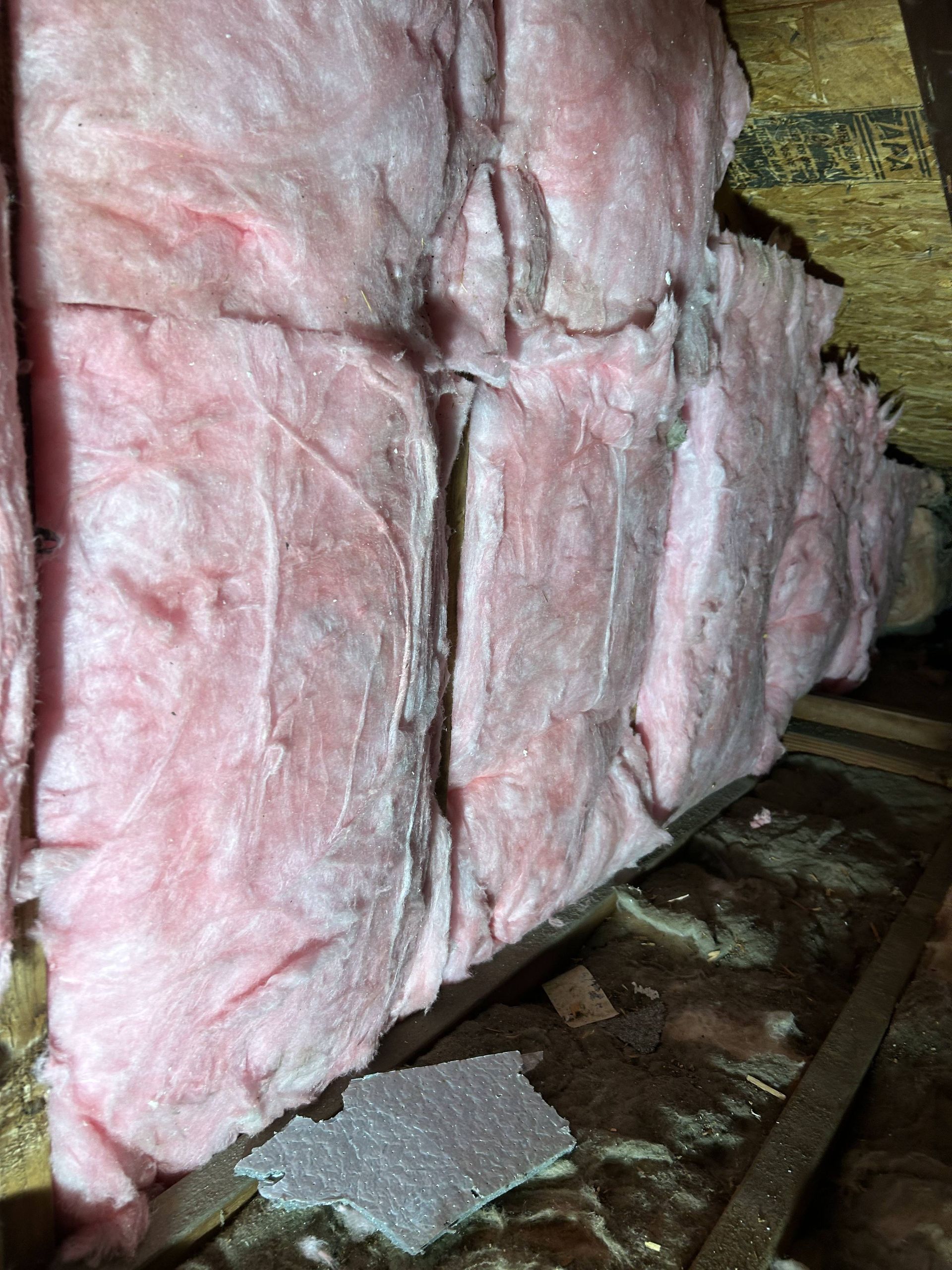 Pink fiberglass insulation in a wall cavity with wooden framing and debris on the floor
