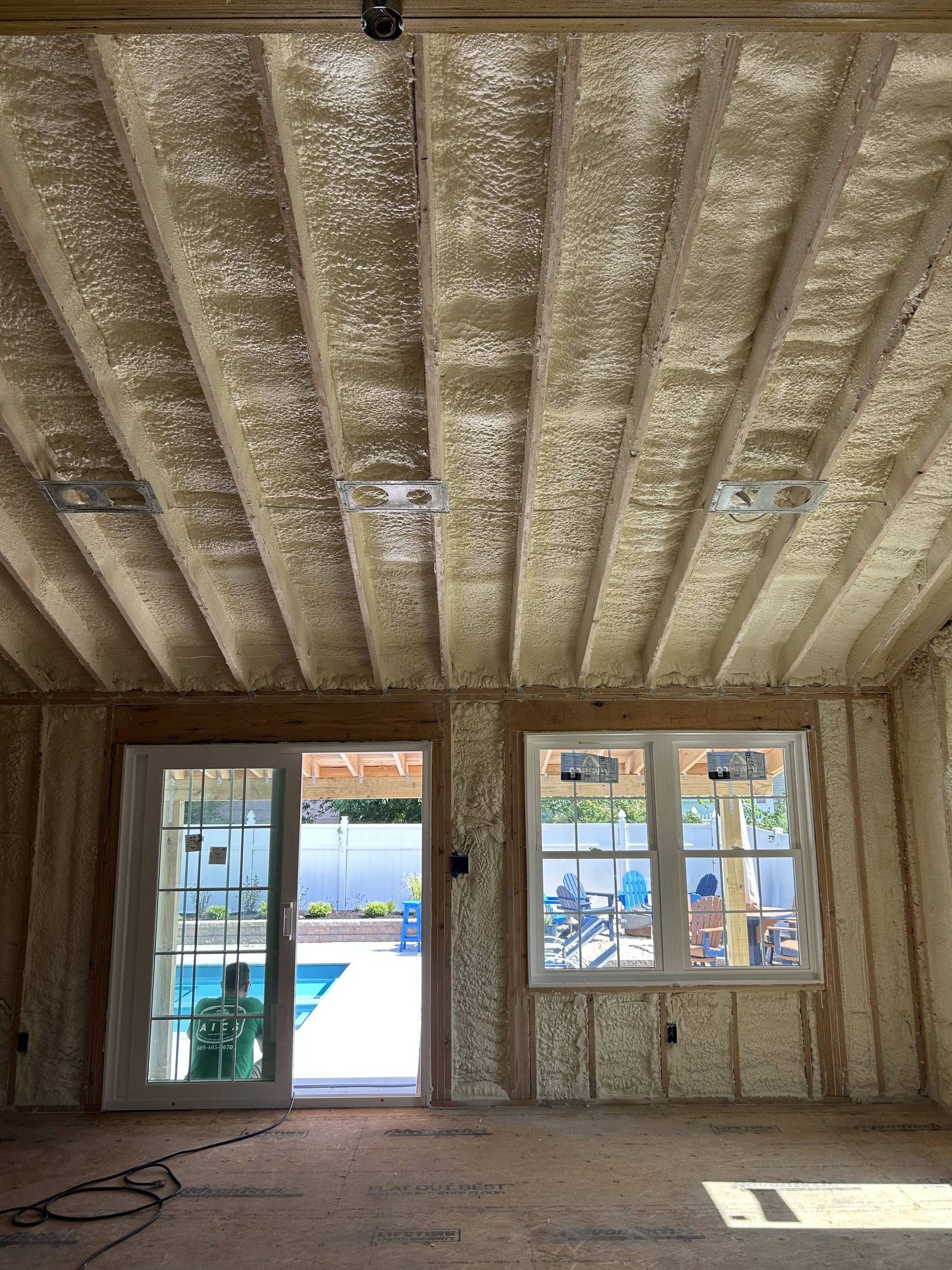 Unfinished room with insulated walls and ceiling, open door to a pool outside, and a window with patio chairs.